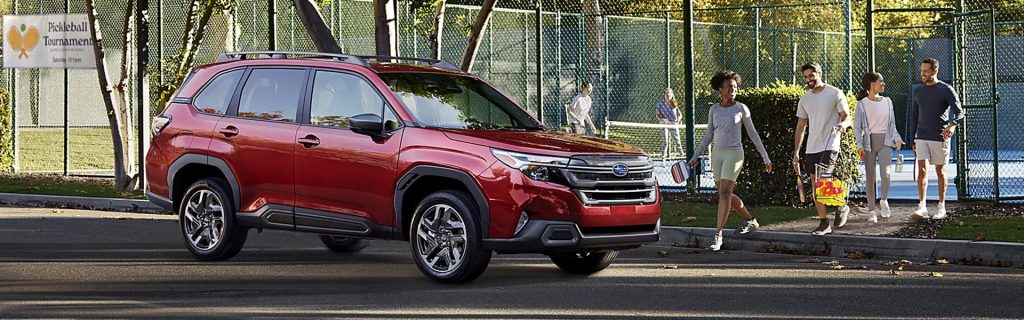 Red 2026 Subaru Forester parked near a pickleball court with people walking in the background.