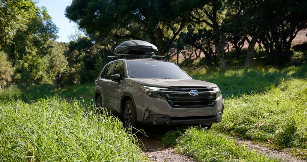A Subaru Outback driving on a dirt path through a forest with a roof cargo box.