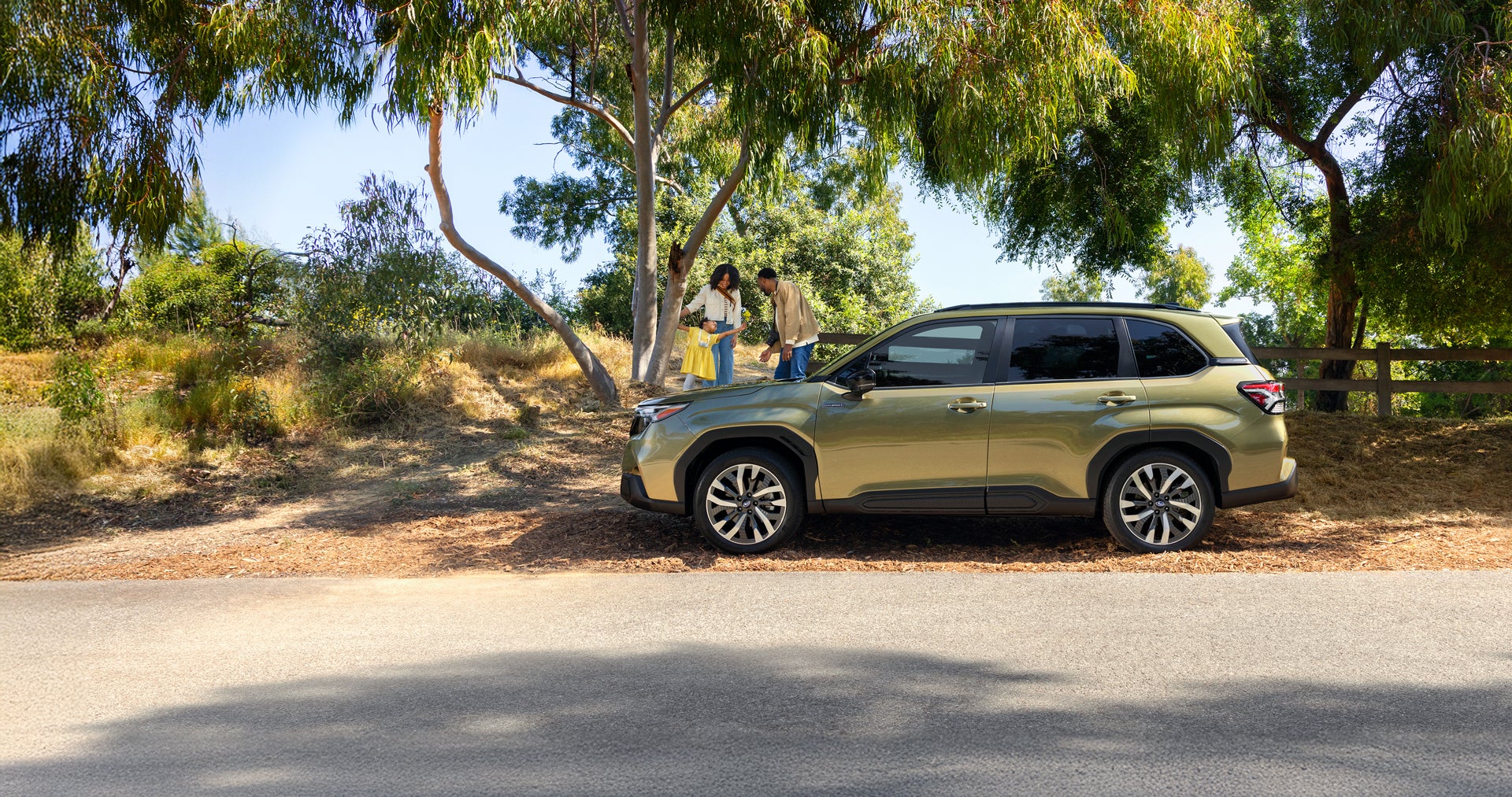 Green Subaru Forester SUV parked under trees with a family standing beside it.
