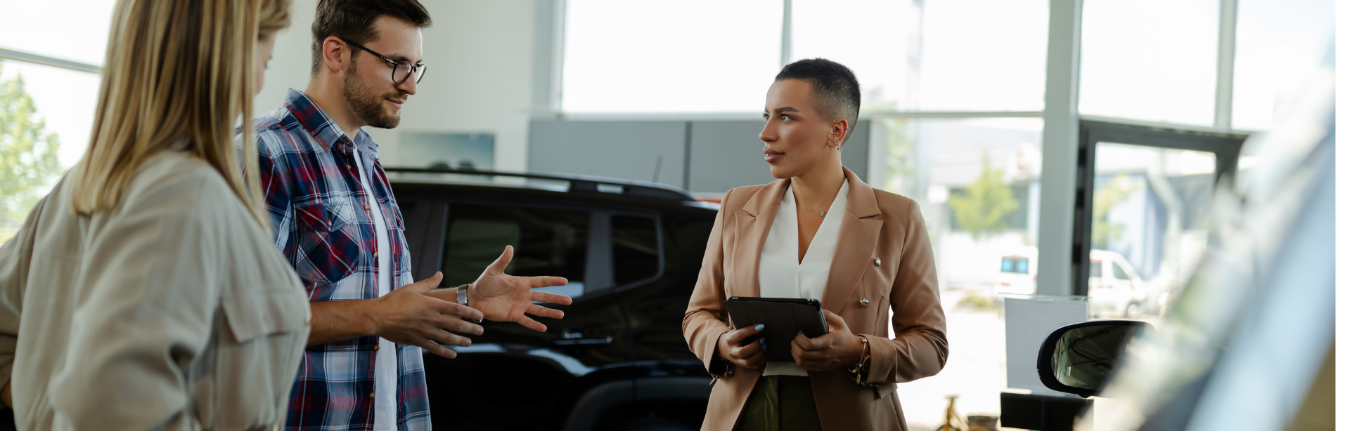 A man and a woman conversing in a car dealership, while another woman looks on.